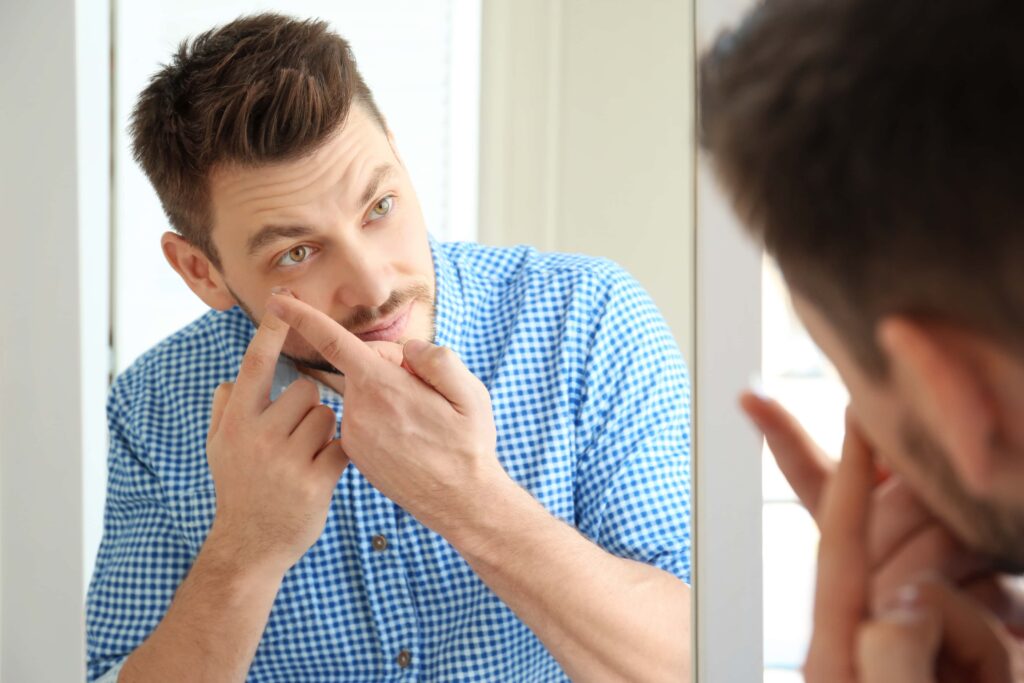 man in plaid shirt testing out contact lenses in front of mirror