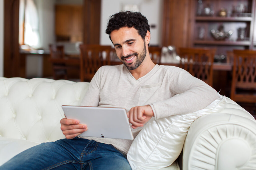 Mixed race adult man smiling while using tablet at home after his LASIK operation