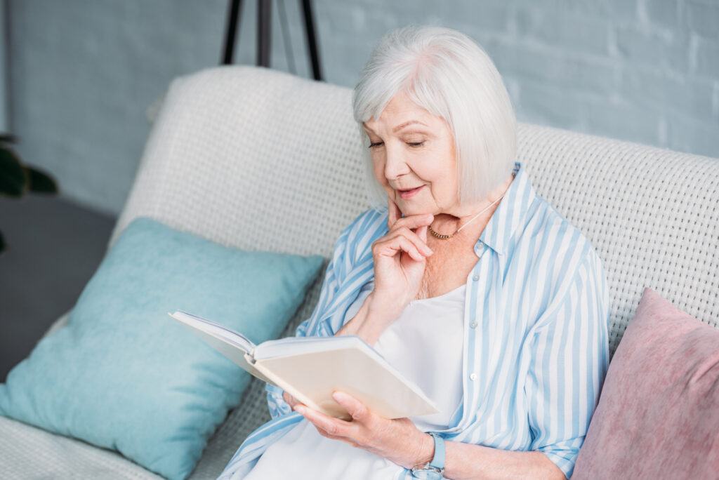 Senior woman reading book while resting on sofa at home