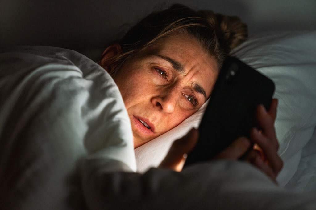 Tired womans eyes being seen as she scrolls through her phone on her bed