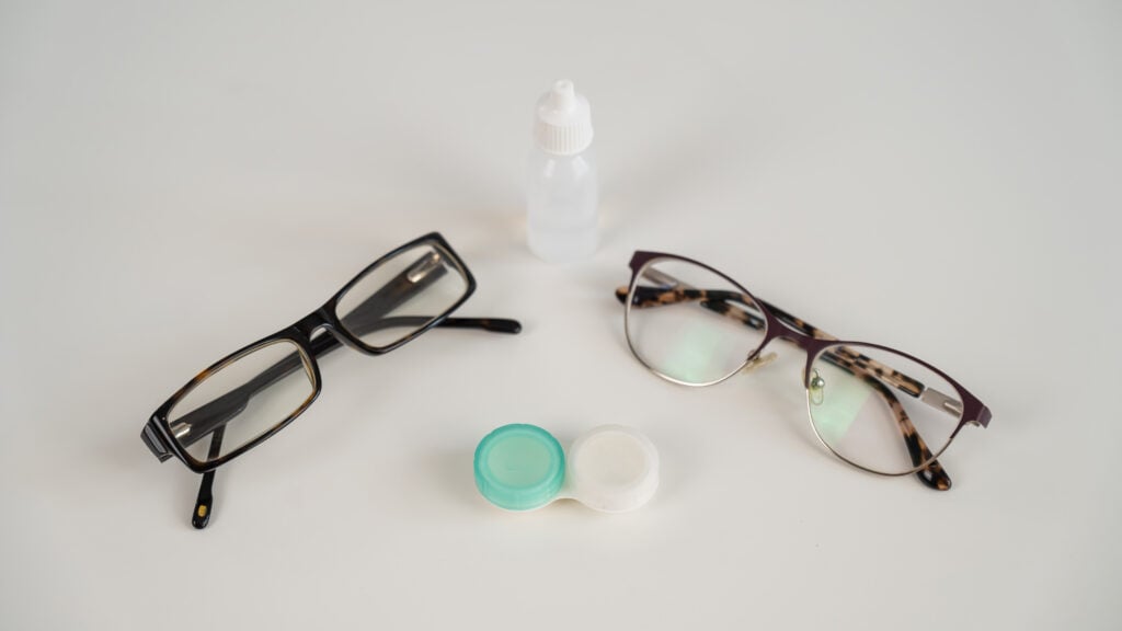 two pairs of glasses lenses and contact drops in the eyes on a white table